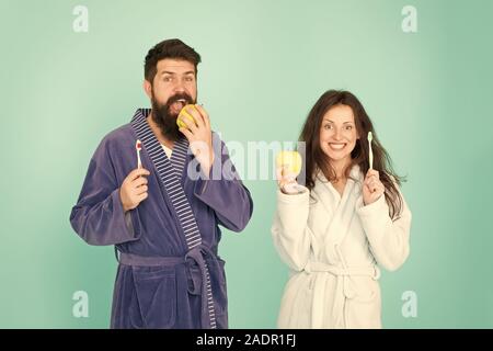 Healthy habits. Brush teeth every morning. Oral hygiene. Couple bathrobes hold toothbrushes and apples. Personal hygiene. Couple in love cleaning teeth. Freshness and cleanliness. Keep teeth healthy. Stock Photo