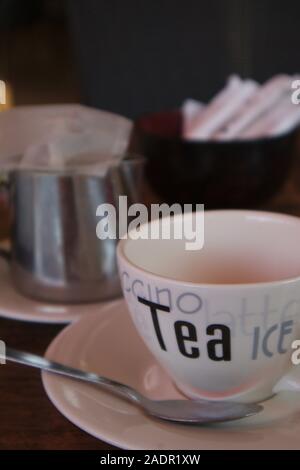 A cup of tea with the teapot in the background and jar with sugar sachets on a restaurant table Stock Photo