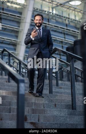 Positive bearded businessman walking down the stairs Stock Photo