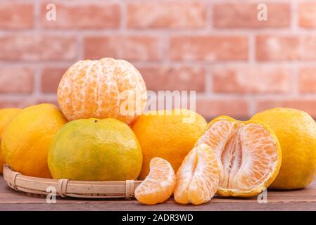 Peeled tangerines in a bamboo sieve basket on dark wooden table with red brick wall background, Chinese lunar new year fruit design concept, close up. Stock Photo