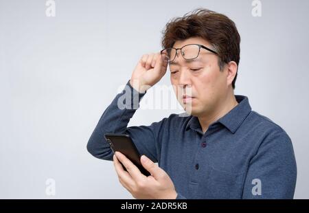 Asian male trying to read something on his mobile phone. poor sight, presbyopia, myopia. Stock Photo