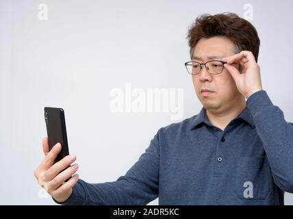 Asian male trying to read something on his mobile phone. poor sight, presbyopia, myopia. Stock Photo