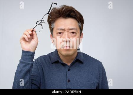 Asian middle-aged male trying to take off glasses and see something. poor sight, presbyopia, myopia. Stock Photo