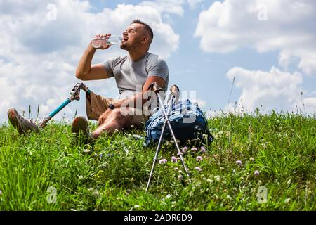 Thirsty young man with prosthetic leg drinking water outdoors Stock Photo