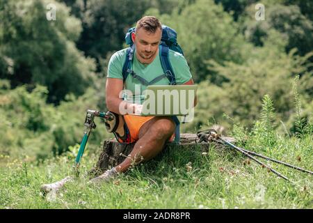 Pleasant young man with prosthesis using his laptop in the forest Stock Photo