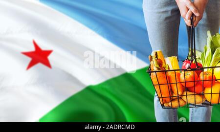 Woman is holding supermarket basket, Djibouti waving flag background. Economy concept for fresh fruits and vegetables. Stock Photo