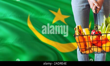Woman is holding supermarket basket, Mauritania waving flag background. Economy concept for fresh fruits and vegetables. Stock Photo