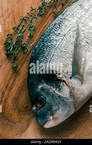 Thyme sprig and raw fish placed on wooden surface Stock Photo