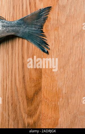 Wet raw fish tail on the wooden cutting board surface Stock Photo