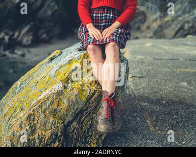 A young woman is relaxing on a rock on the coast in the autumn