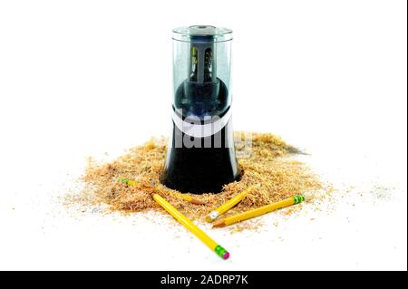 An electric pencil sharpener surrounded by pencil shavings and a few pencils lying at the bottom, isolated on white background Stock Photo
