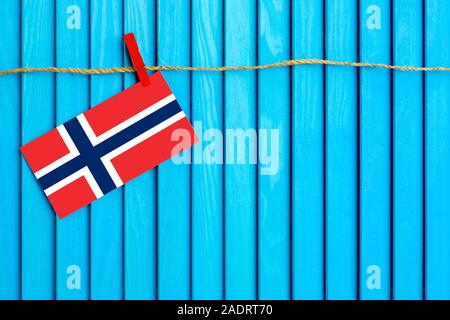 Flag of Norway hanging on clothesline attached with wooden clothespins on aqua blue wooden background. National day concept. Stock Photo