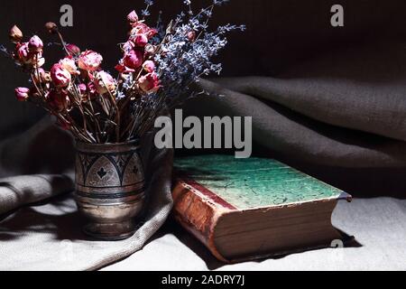 Vintage still life with bouquet of dried flowers in a silver vase near old book Stock Photo