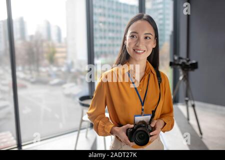 Dark-haired young cute reporter holding a camera Stock Photo