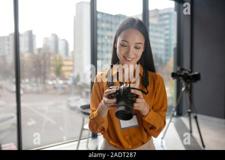 Dark-haired young cute reporter watching photos in camera