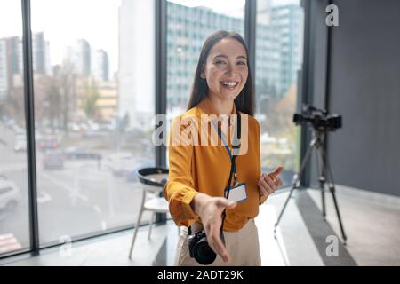 Dark-haired young cute reporter with camera smiling positively Stock Photo