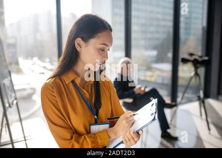 Young beaming pretty asian reporter making notes Stock Photo