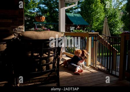 Toddler boy hugs basset hound dog on deck in backyard at home Stock Photo