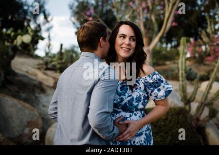 Husband Hugging Pregnant Wife as She Smiles Stock Photo