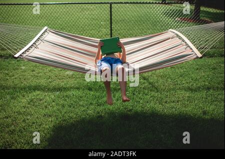 Boy 7-8 years old watching his tablet while laying in hammock outdoors Stock Photo