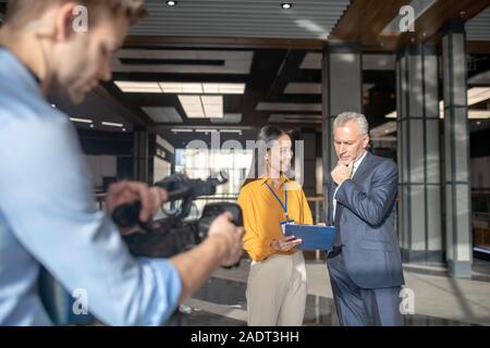 Asian female reporter in beige pants making motes Stock Photo