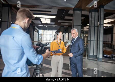 Asian female reporter standing next to grey-haired man Stock Photo