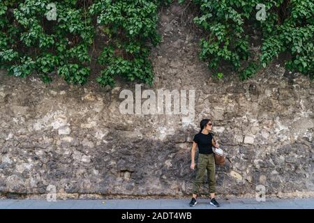 Active young woman with her bag hanging, next to a stone wall looking