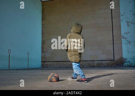 Boy with his hands in his pockets next to a deflated basketball ball. Stock Photo