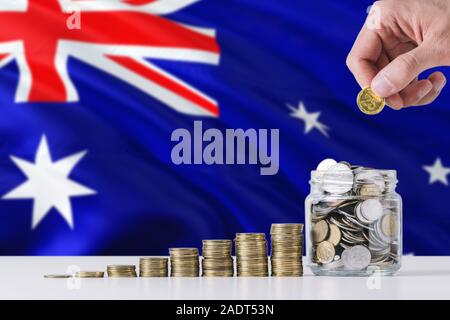 Business man holding coins putting in glass, Australia flag waving in the background. Finance and business concept. Saving money. Stock Photo