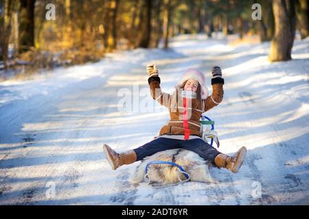 Girl playing and having fun in the winter forest at sunset. Children sledding in a snowy park. Winter holiday. Stock Photo