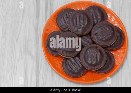 Jaffa cakes biscuits stacked on an orange plate.  On a grey wood surface. Stock Photo