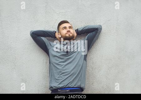 Bearded man holding hands behind head dreaming on a gray background. Stock Photo