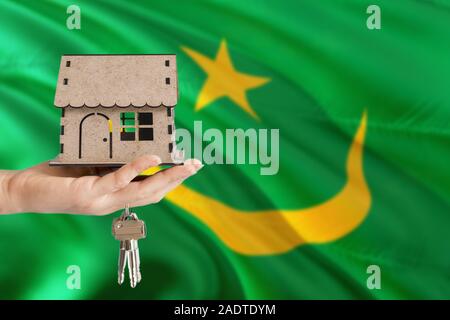 Woman hand holding wooden house and keys with hand. Mauritania flag with concept of rent, purchase, insurance, building real estate, eco house. Stock Photo