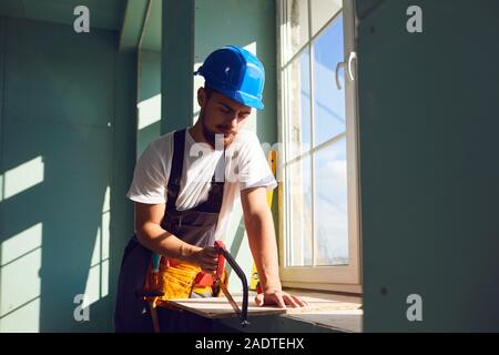 Builder contractor bearded man in helmet smiling while standing at a construction site. Stock Photo