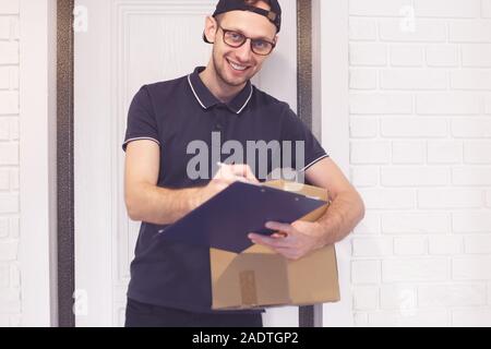 Young man courier, delivered the parcel, signs the document smiling Stock Photo