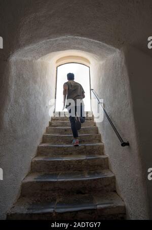 Man running away up a steep flight of stone stairs towards daylight through an arched exit at the top viewed from below Stock Photo