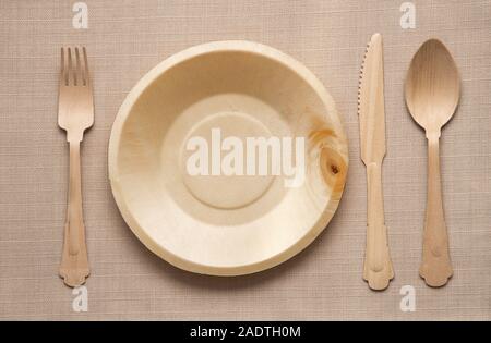 Wooden cutlery and matching empty clean plate viewed in a flat lay from above in a table setting on a woven beige linen fabric Stock Photo