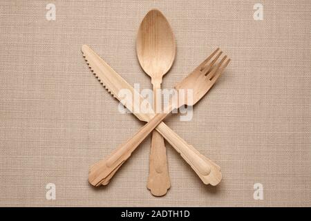 Set of handcrafted wooden cutlery in a star arrangement with the knife and fork crossed over the spoon on a textured beige fabric background Stock Photo