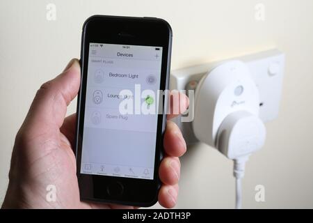 A man turning on a light via a smart plug with an app on his phone. Stock Photo