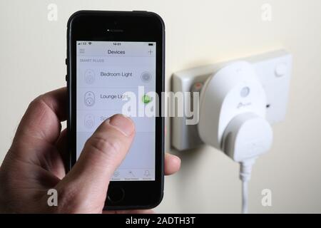 A man turning on a light via a smart plug with an app on his phone. Stock Photo