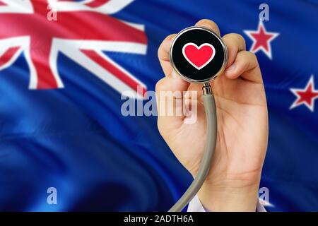 Doctor holding stethoscope with red love heart. National New Zealand flag background. Healthcare system concept, medical theme. Stock Photo