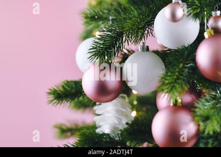 Close up of decorated Christmas tree with white seasonal and pink tree ornaments like baubles and stars on pink background with lights in background Stock Photo