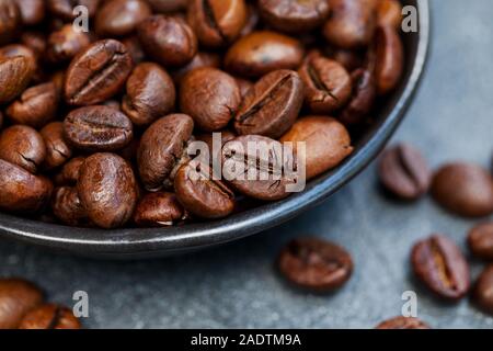 Coffee beans close up shot in black bowl on grey slate background. Close up Stock Photo