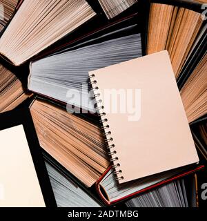 The e-book with a white screen lies on the open multi-colored books that lie on a dark background, close-up Stock Photo
