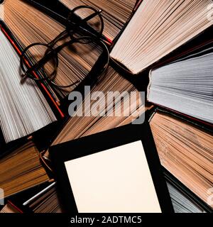 The e-book with a white screen lies on the open multi-colored books that lie on a dark background, close-up Stock Photo