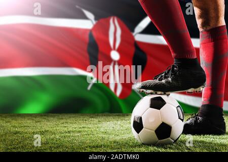 Close up legs of Kenya football team player in red socks, shoes on soccer ball at the free kick or penalty spot playing on grass. Stock Photo