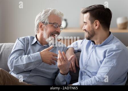 Aged father talking with grownup son family sitting on couch Stock Photo