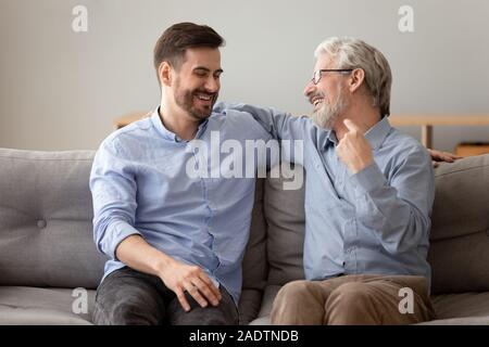 Old father grownup son laughing having fun sitting on sofa Stock Photo