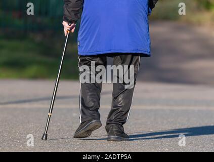 View from behind of an elderly man walking using a walking stick as a reduced mobility walking aid. Stock Photo
