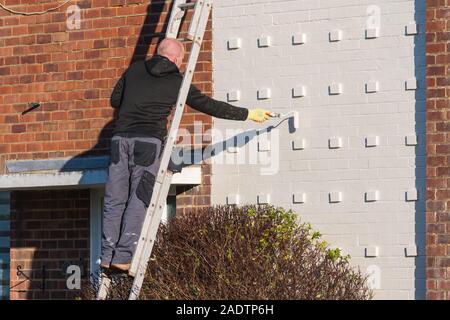Man up a ladder painting and decorating the exterior of a house using a roller brush. Stock Photo
